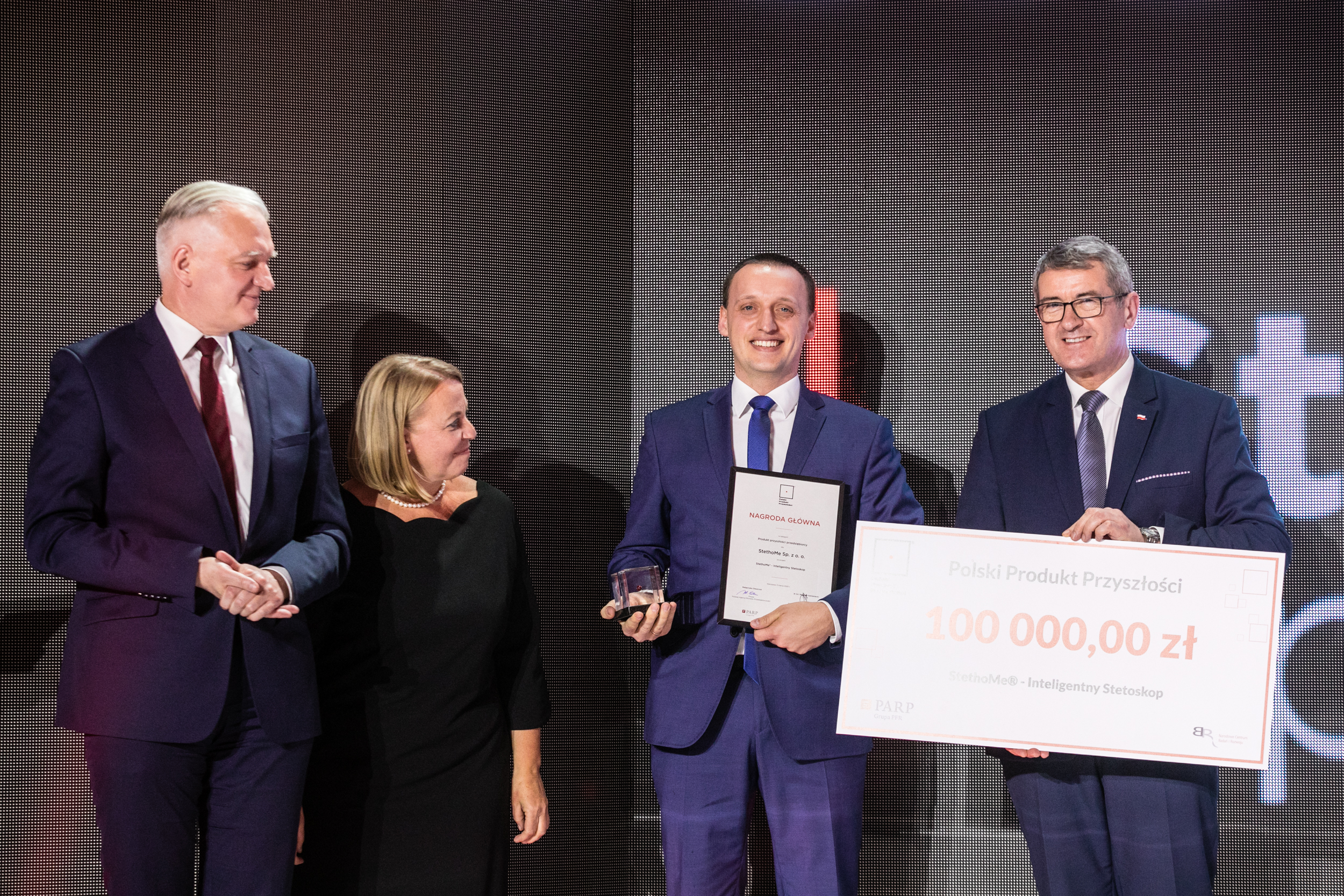 na zdjęciu Jarosław Gowin, Małgorzata Oleszczuk oraz Wojciech Murdzek wręczają szklaną statuetkę oraz czek na 100 000,00 zł młodemu mężczyźnie