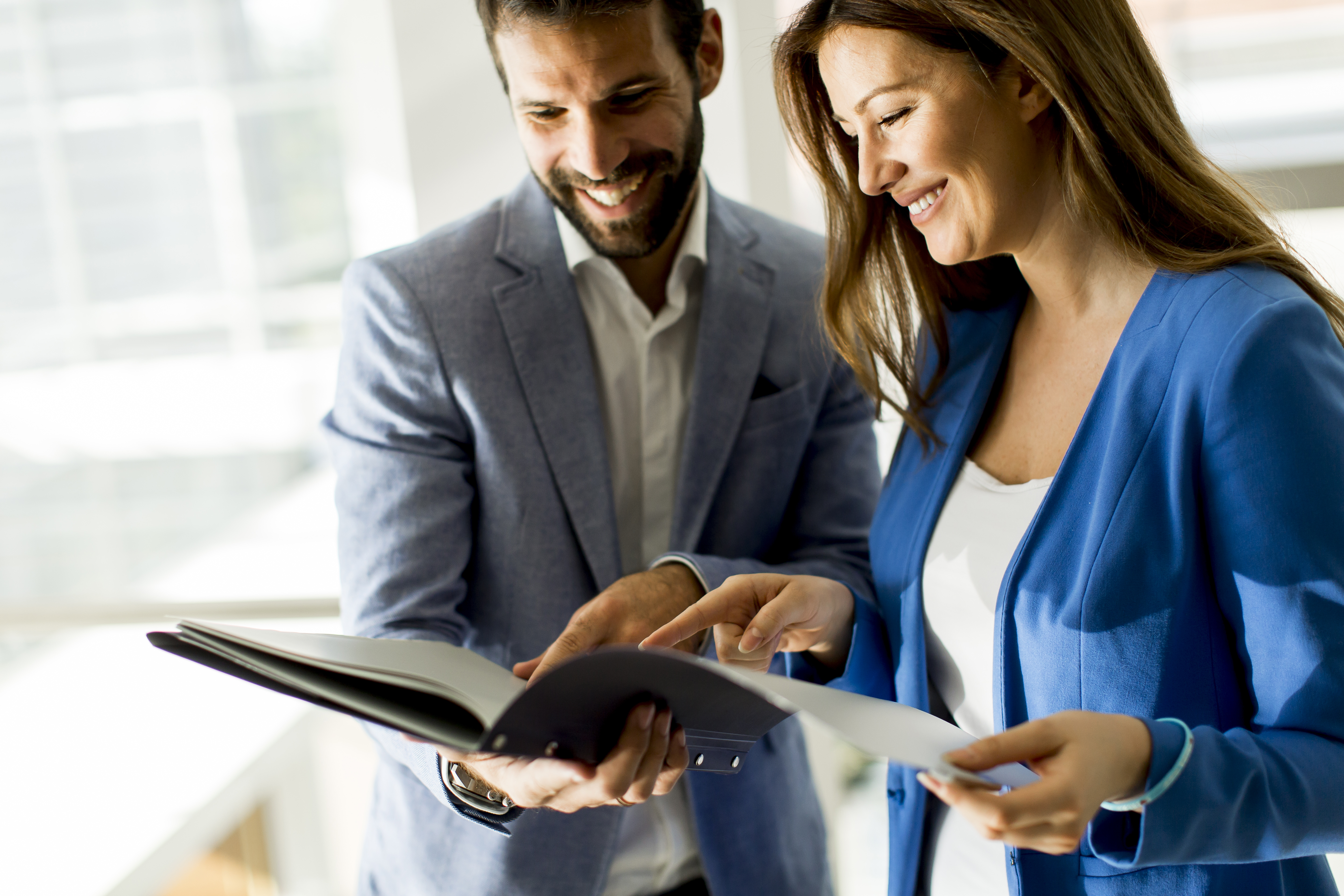 Młoda kobieta i mężczyzna trzymają wspólnie segregator i patrzą się na zawartości 