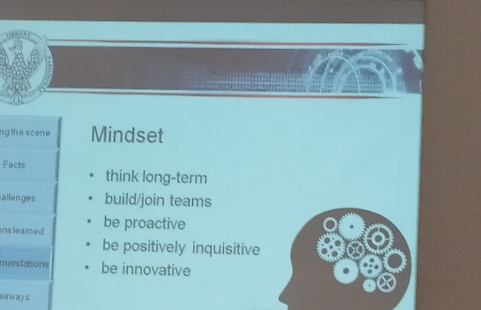 widok na jeden ze slajdów prezentacji. Widać na nim napisy: mindset, think long-term, build/join teams, be proactive, be postively inquisitive, be innovative. W prawym dolnym rogu widać piktogram przypominający głowę człowieka, a na niej symbole przypominające tryby