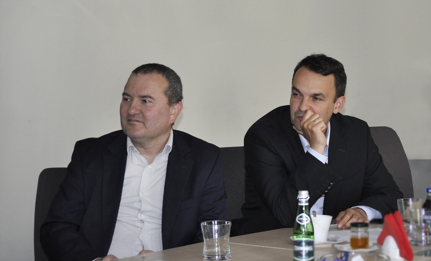 dwóch mężczyzn ubranych w garnitury siedzi przy stole