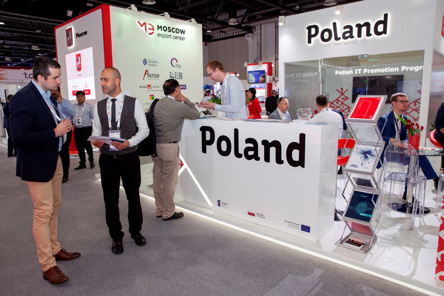 Młodzi mężczyźni stoją w hali przy białym kiosku z czarnym napisem Poland