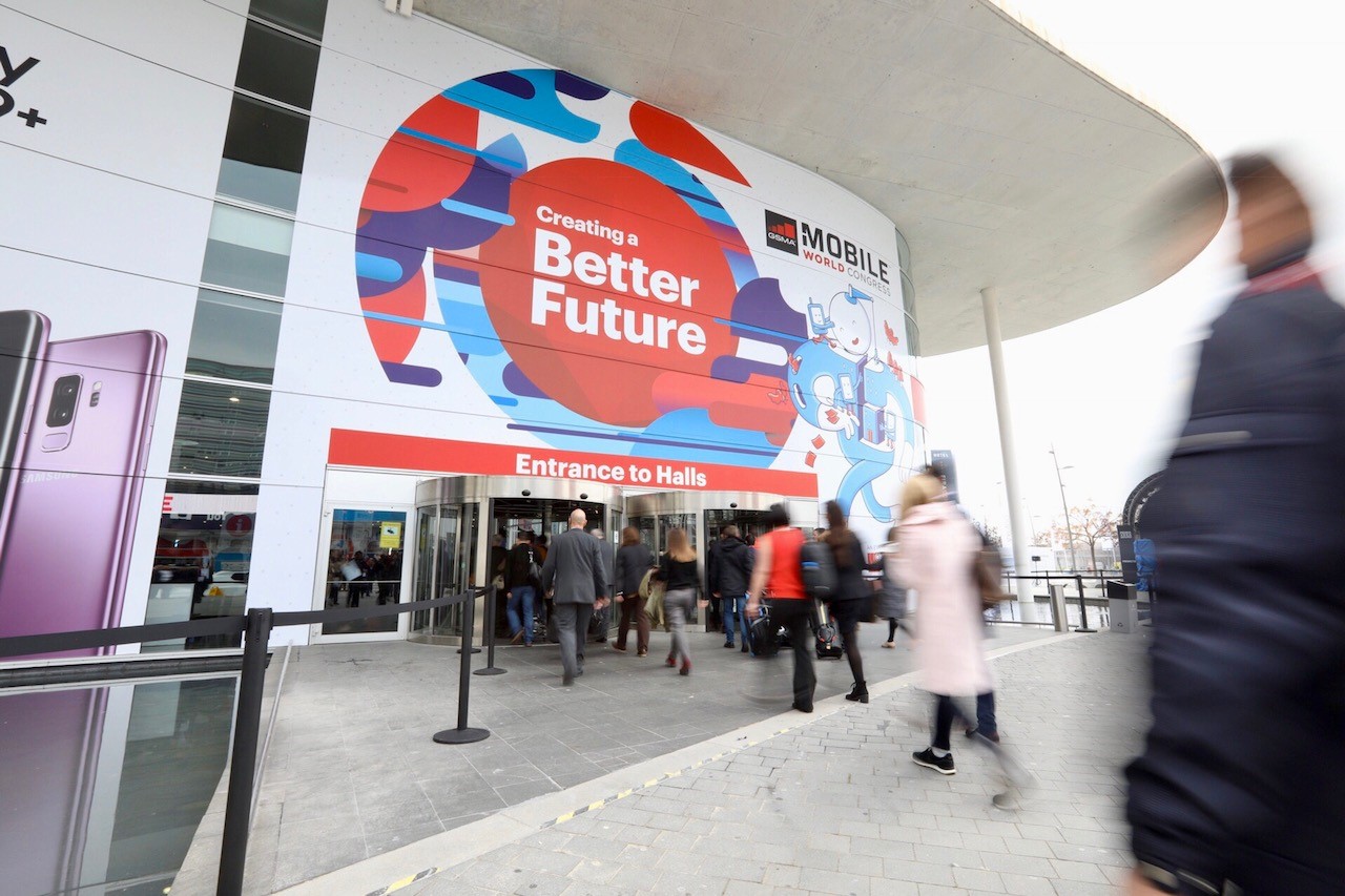 Zbliżenie na wejście do budynku. Widać kobiety i mężczyzny zmierzających do wejścia. Nad wejściem...