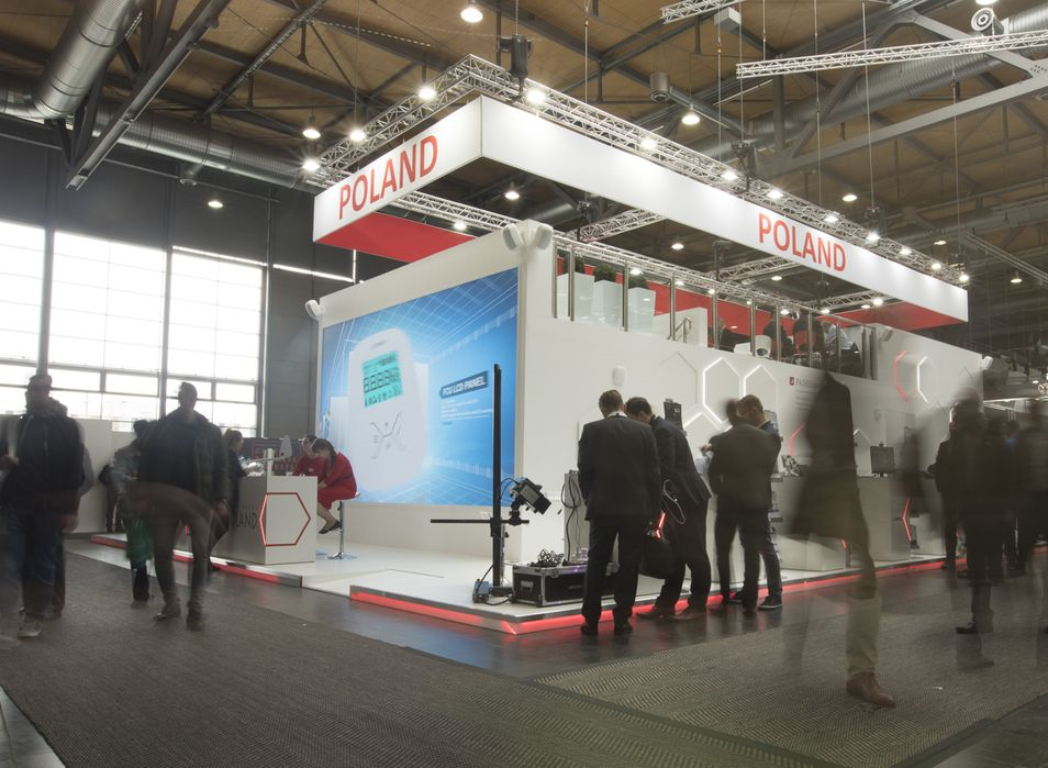 Zdjęcia przedstawia wnętrze hali, w której stoi konstrukcja o białych ścianach i podwieszanym na...