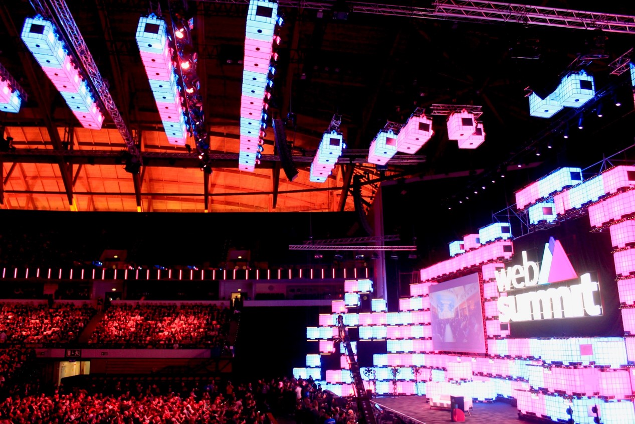 Widok na trybuny oraz scenę znajdujące się w hali goszczącej wydarzenie Web Summit. Na trybunach i...