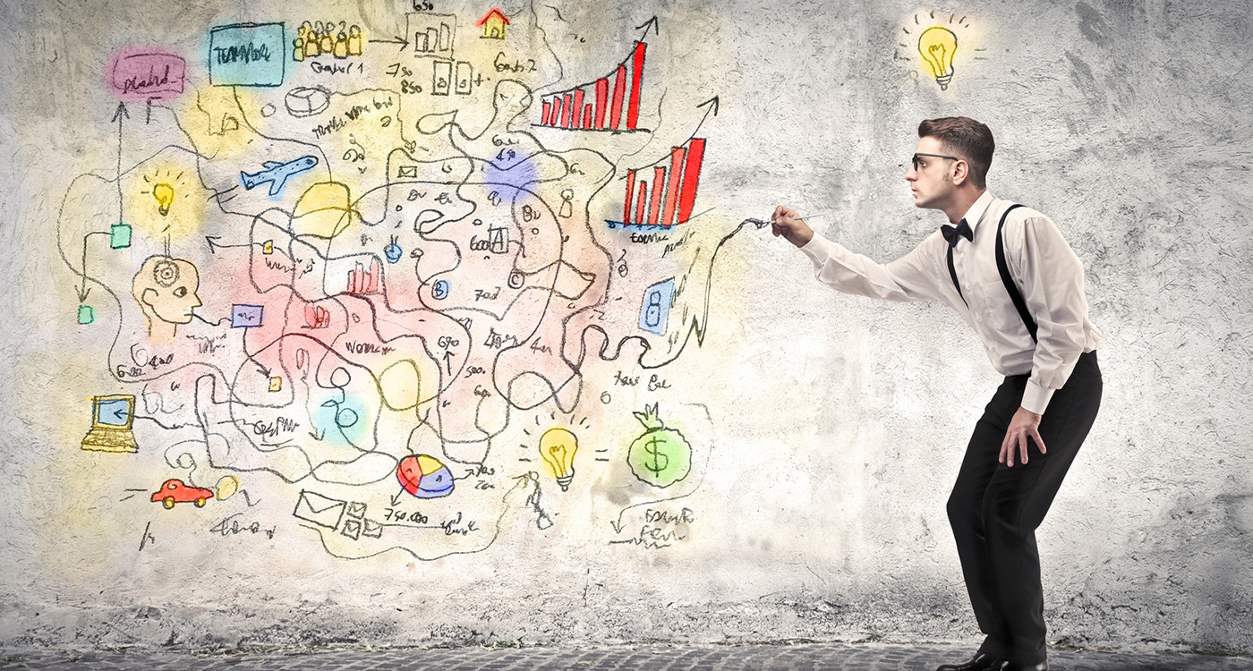 Młody mężczyzna w okularach rysuje na ścianie wykresy i różne symbole