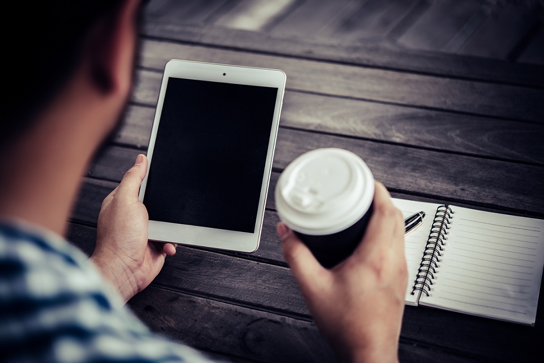 Widok z góry na mężczyznę w młodym wieku, który siedzi przy stoliku i w jednej ręce trzyma biały...