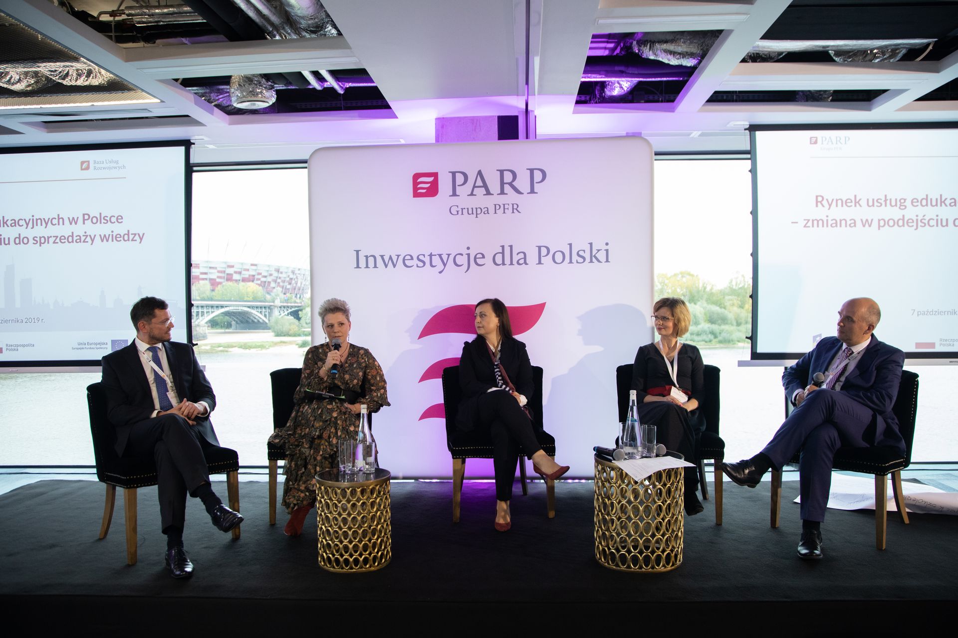 Prelegenci siedzący pod ekranem do prezentacji w czasie konferencji