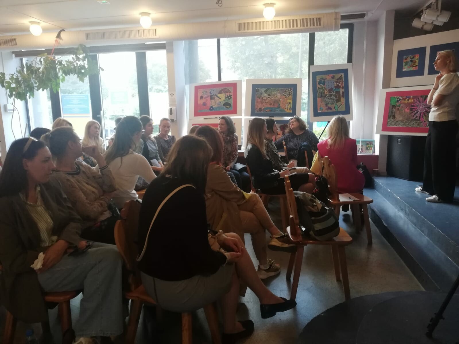 Na zdjęciu widać grupę kobiet siedzących w sali, po prawej stronie kobieta prowadzi wykład