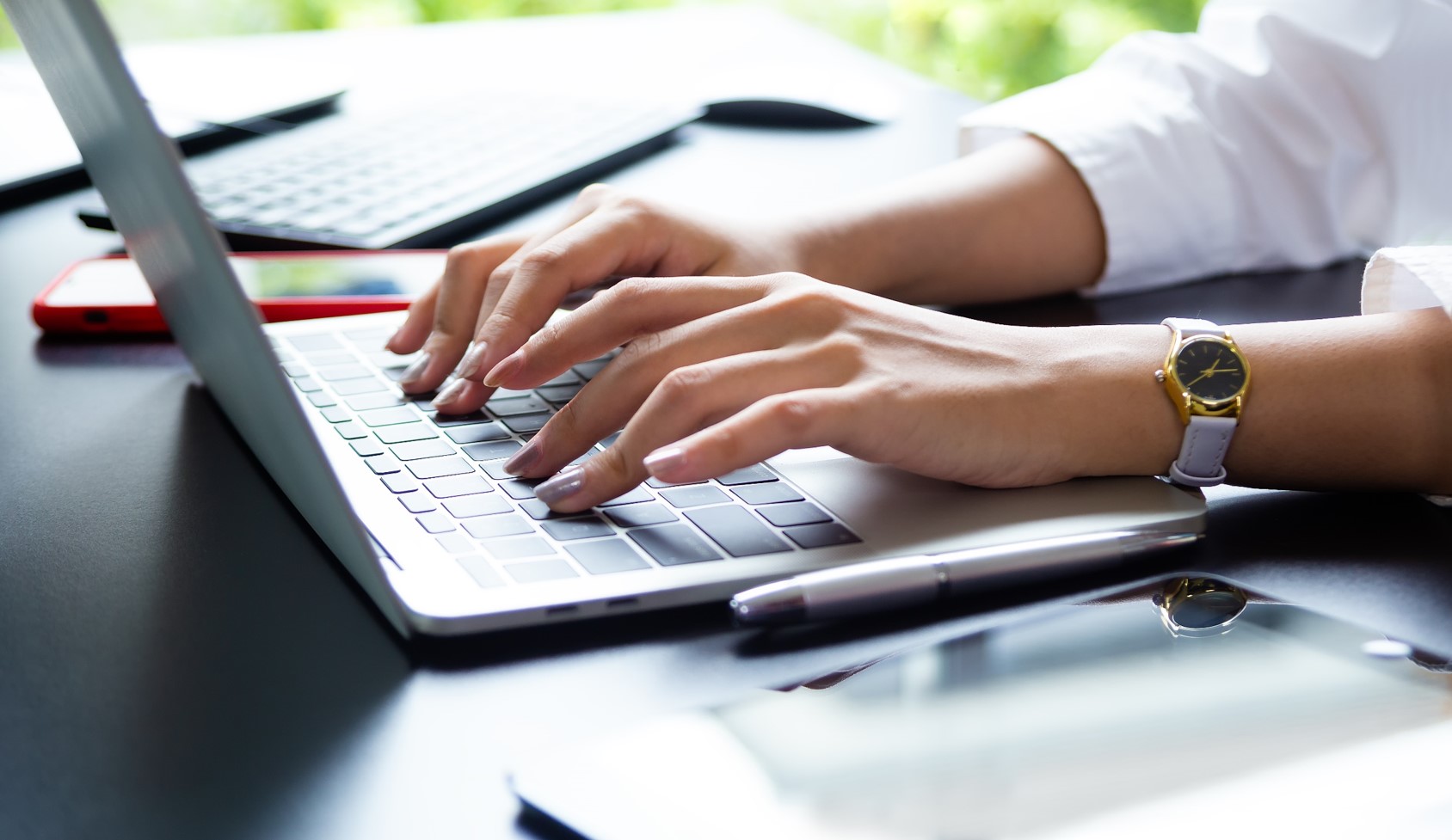 Zdjęcie przedstawia zbliżenie na dłonie kobiety, która pracuje przy laptopie. 