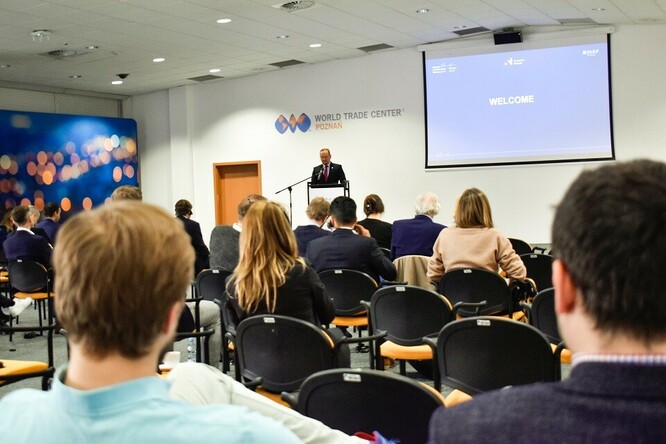 Ludzie siedzący na sali patrzą na osobę przemawiającą z mównicy