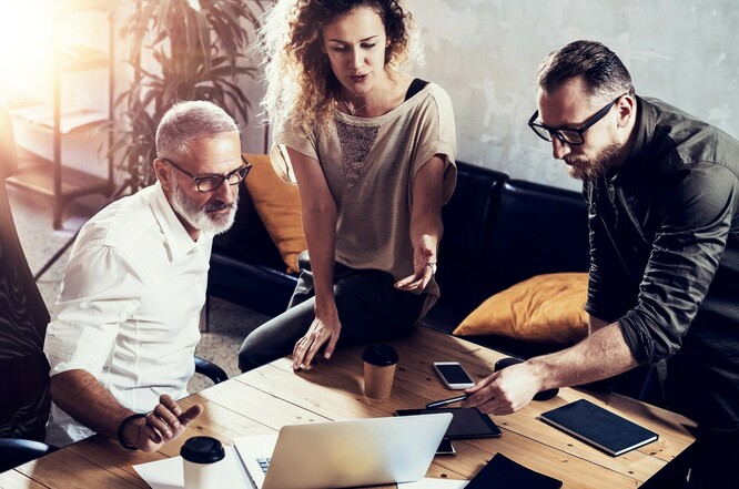 Dwóch mężczyzn i kobieta siedzą przy stole i patrzą się w ekran laptopa