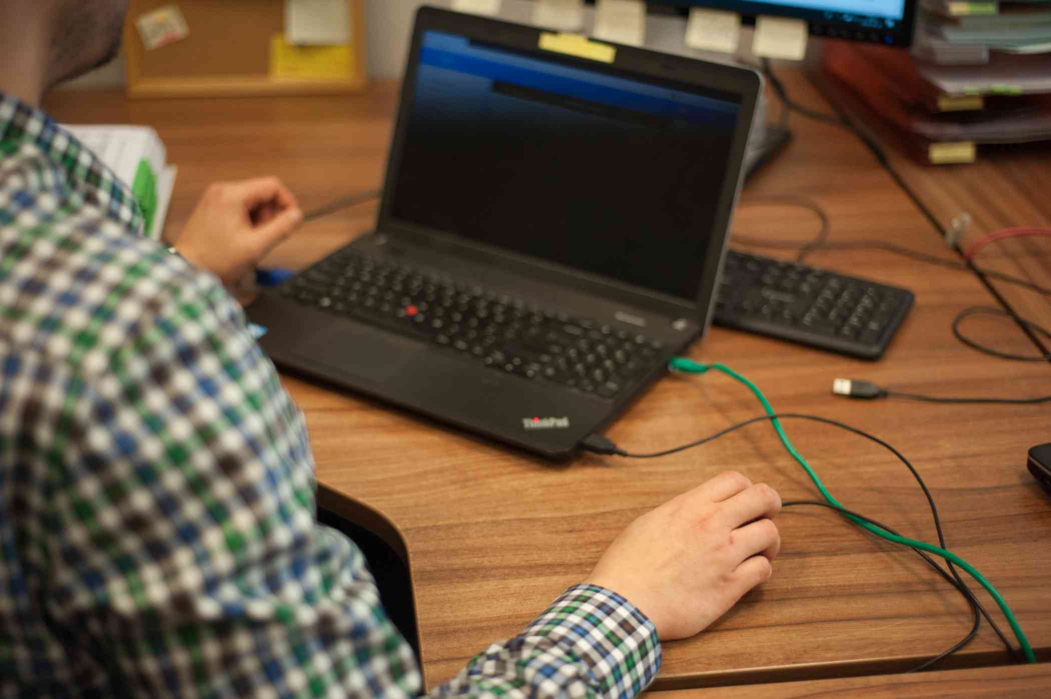 Laptop stojący na biurku, widok ręki, która trzyma mysz komputerową i robi coś na komputerze