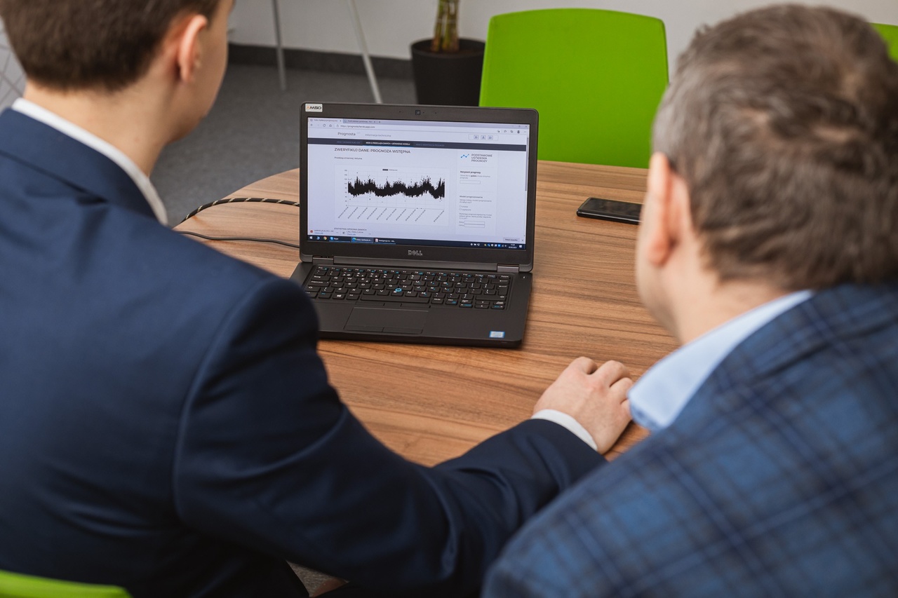 LAptop na stole, przed nim dw&oacute;ch mężczyzn