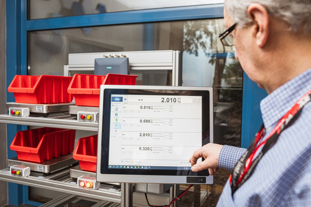 Pojemniki stojące na pólkach, przy nich monitor